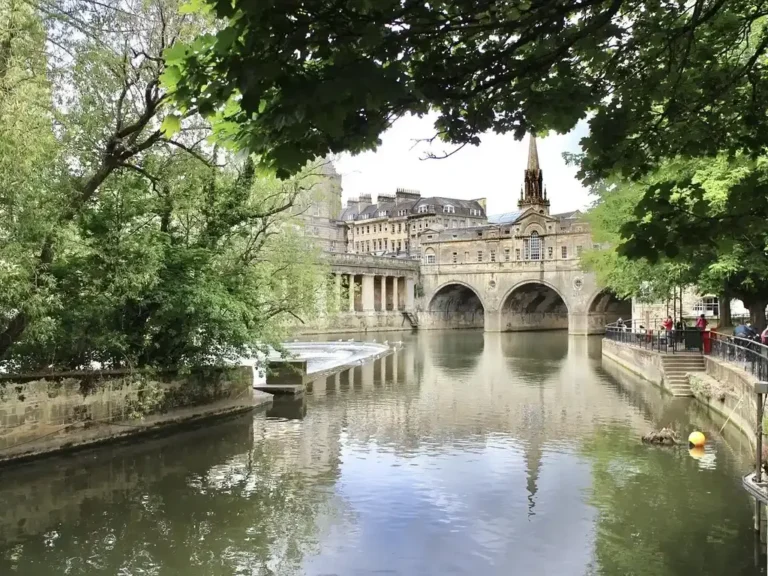 Pulteney Bridge and a church spire of Bath framed by trees on the River Avon