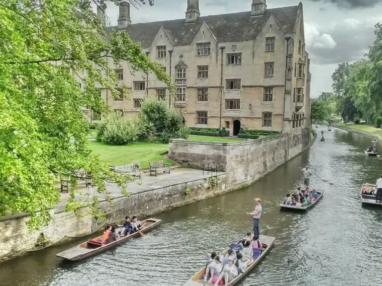 Punts full of visitors passing a Cambridge college on the River Cam