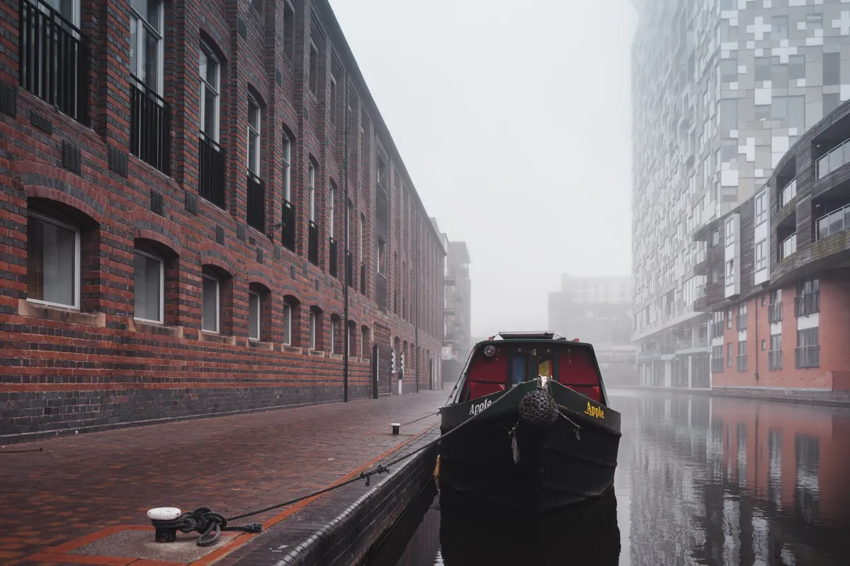 Narrowboat on a misty Birmingham canal beside modern buildings