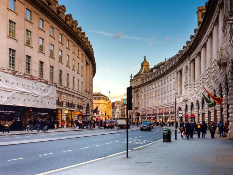 The curved Regency facades of Regent Street in London at dusk with shoppers on the pavement